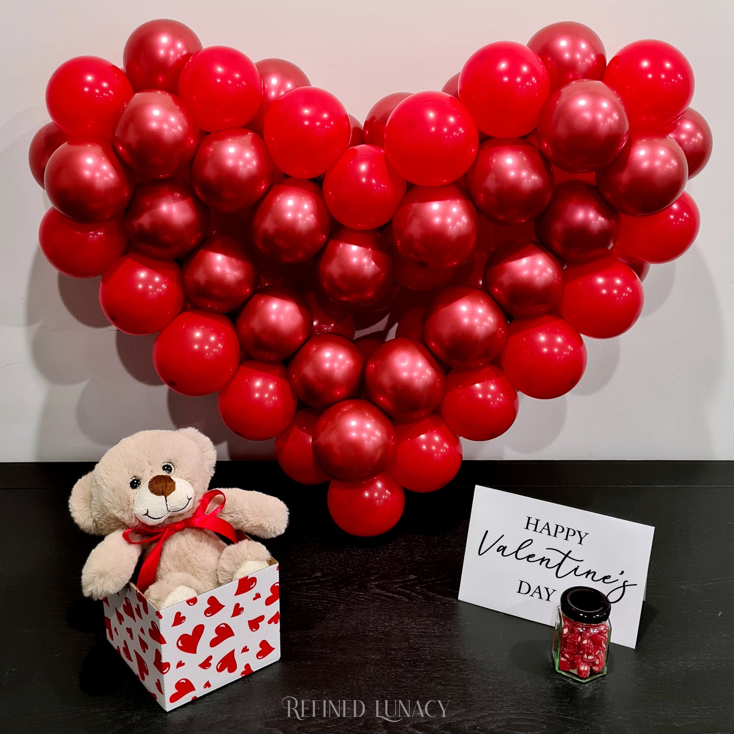 Red balloon garland with plush teddy bear in heart box with Happy Valentine's Day card and heart rock candy